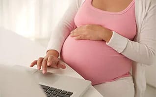 home-blog-image-left pregnant woman with hand on belly working at laptop